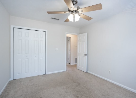 an empty living room with a ceiling fan and a closet
