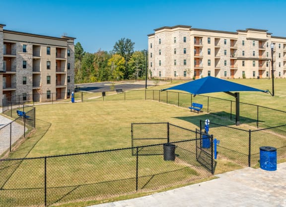 a fenced in dog park with agility courts in front of apartment buildings