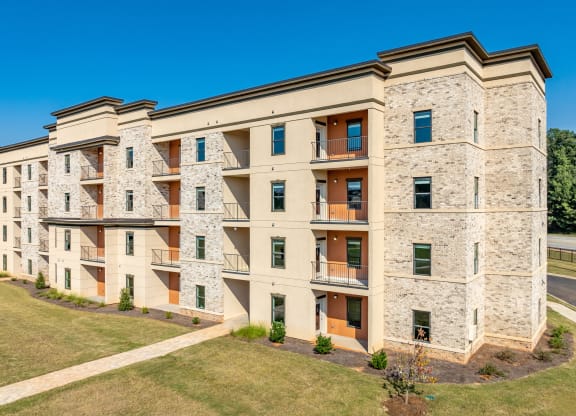 a large apartment building with brick and stone facade and a lawn