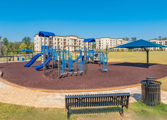 a playground with blue playset and umbrellas in front of apartments