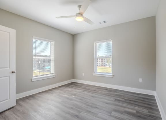 an empty living room with a ceiling fan and two windows