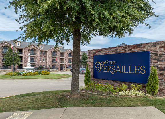 a sign for the versailles on the side of a brick building with a tree