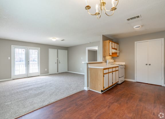 an empty living room with a kitchen and a chandelier