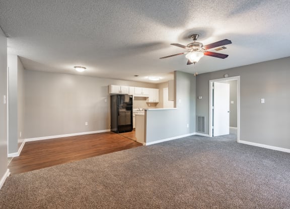 an empty living room with a ceiling fan and a kitchen