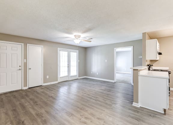 an empty living room with a kitchen and a ceiling fan