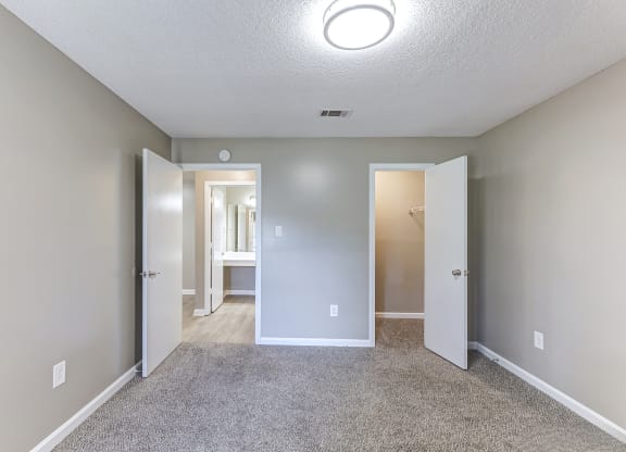 an empty room with a hallway to the bathroom and an open door to the bedroom
