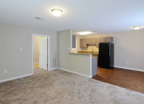 an empty living room and kitchen with a black refrigerator