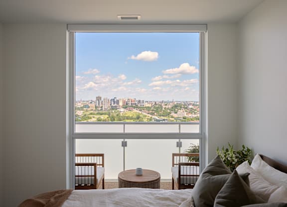 A bedroom with a large window overlooking a cityscape.