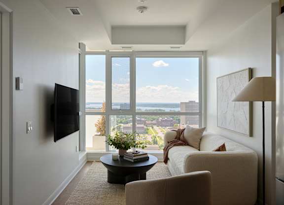A living room with a flat screen TV mounted on the wall and a large window with a view of the city.