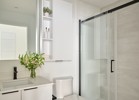 A white toilet sits in a modern bathroom next to a sink and a glass shower door.