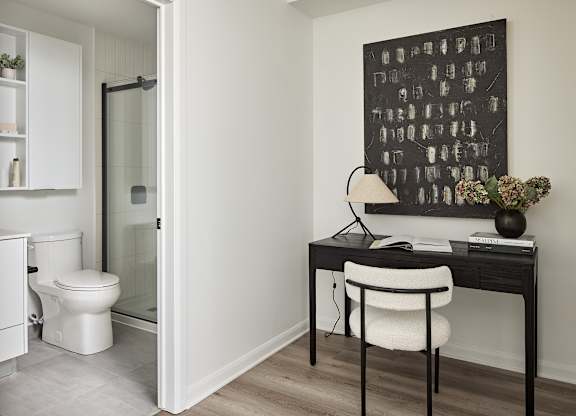 A bathroom with a toilet and a desk with a chair.