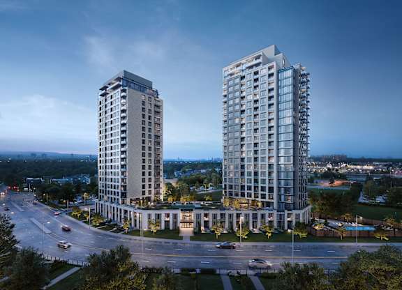 Two modern high-rise buildings are situated in a roundabout with a road and cars passing by.