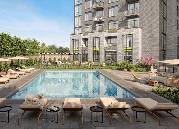 A large pool surrounded by lounge chairs and umbrellas in front of a building.