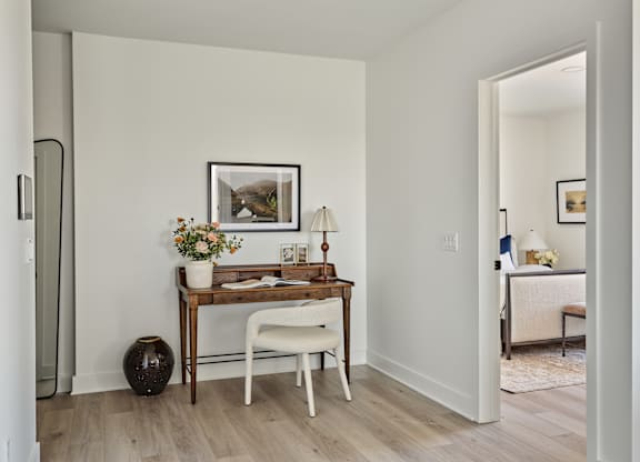 A room with a desk, chair, and vase on the floor.