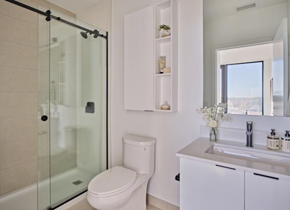 A modern bathroom with a glass shower door, white toilet, and a white sink with a mirror above it.
