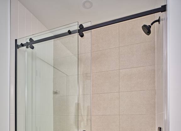A glass shower door with a black handle and a drain in the tub.