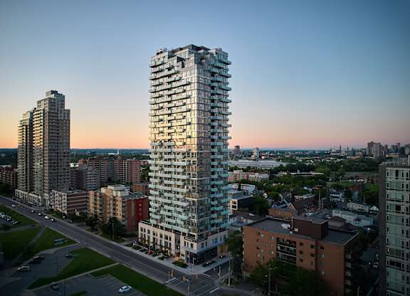 A tall, modern glass building stands in the foreground of a cityscape at dusk.