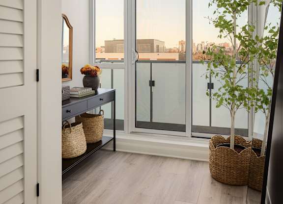 A room with a sliding glass door leading to a balcony with a tree in a pot.