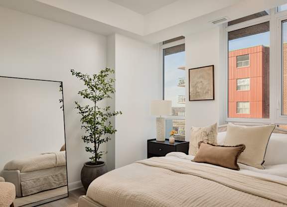 A bedroom with a large bed, a chair, a potted plant, and a mirror.
