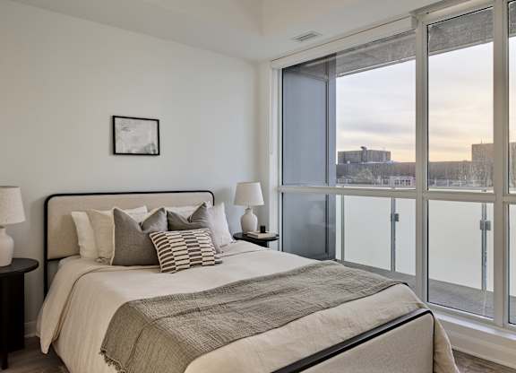 A bedroom with a large bed, a nightstand with a lamp, and a picture on the wall.