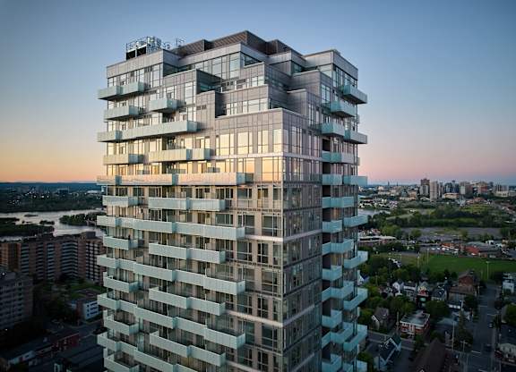 A tall, modern building with many windows and balconies is shown from a distance.