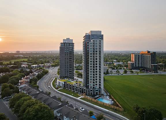 Two tall buildings are situated in a green field with a road running in between them.