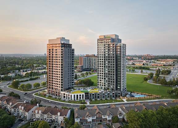 Two tall buildings are surrounded by a green field and smaller buildings.