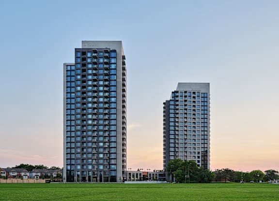 Two modern high-rise buildings with glass windows are situated in a grassy area.
