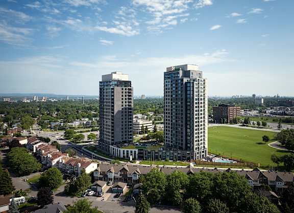 Two tall buildings are surrounded by a green field and houses.