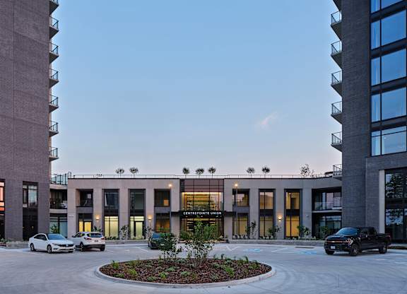 A modern building with a circular garden in front and cars parked outside.