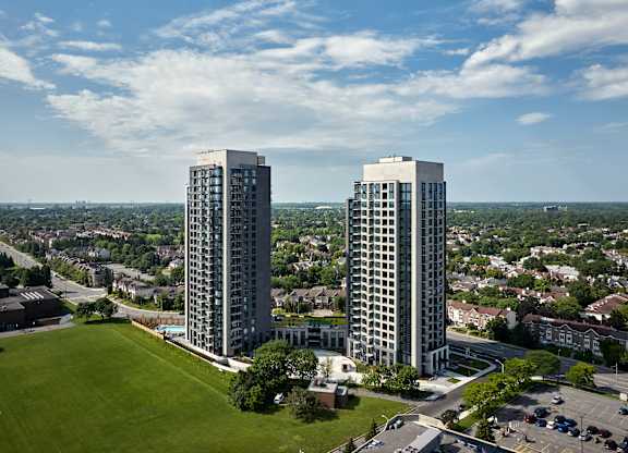 Two tall buildings are surrounded by a green field and a parking lot.