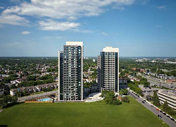 Two tall buildings are surrounded by a green field.