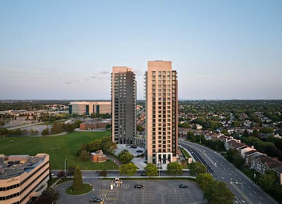 Two tall buildings are situated in a parking lot with a road in between them.