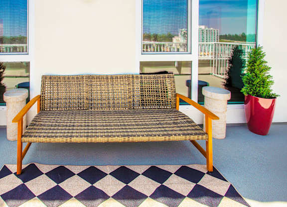 A wicker sofa sits on a checkered rug in front of two red planters.