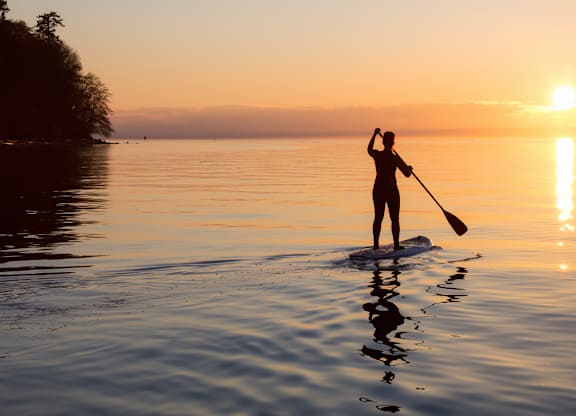 A person paddling a kayak on a calm body of water during sunset.