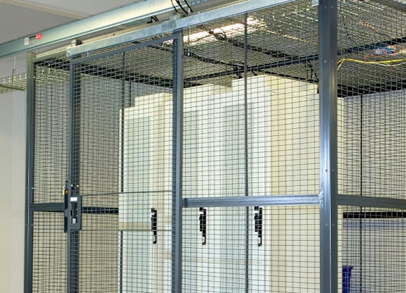 A metal mesh fence encloses a white cabinet.