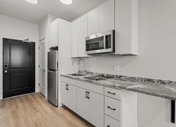 an apartment kitchen with white cabinets and granite counter tops and a black refrigerator and microwave