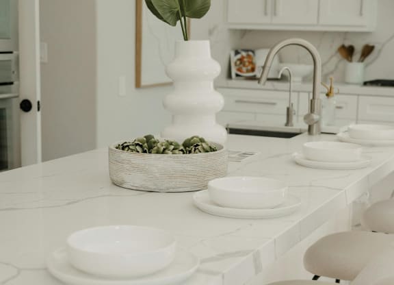 A white kitchen with a basket of green leaves on the counter.
