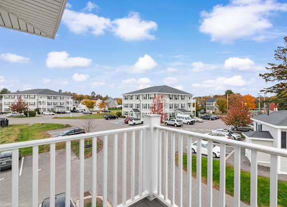 A white railing overlooks a parking lot and apartment buildings.