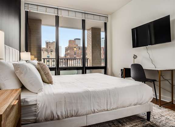 A bedroom with a large bed, a chair, and a flat-screen TV mounted on the wall.