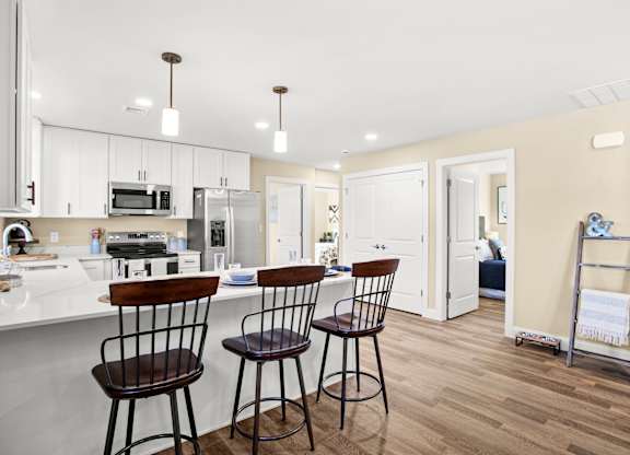 a kitchen with white cabinets and a bar with three stools