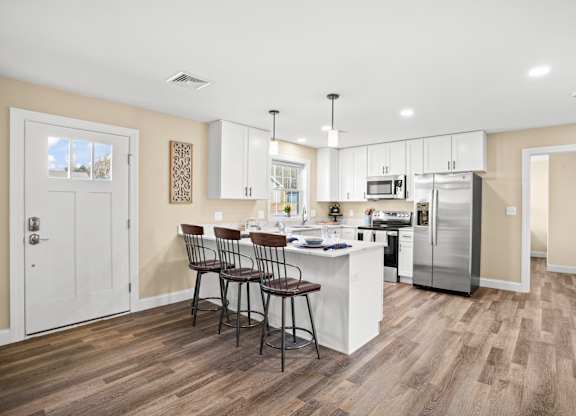 a kitchen with white cabinets and a white island with three chairs
