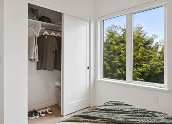 a bedroom with a large window and a closet with clothes