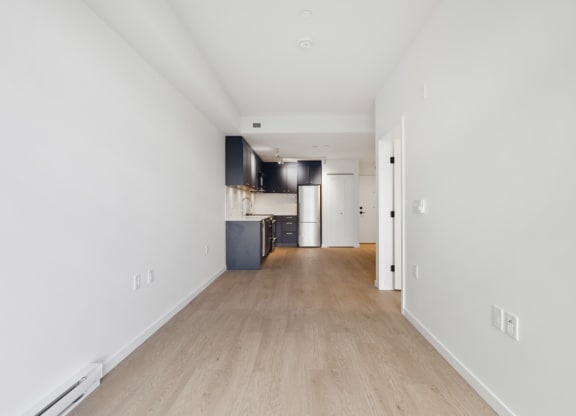 the living room and kitchen of an apartment with white walls and wood floors