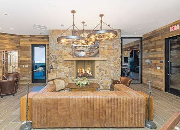 A large bed with a wooden headboard is in the center of a room with a stone fireplace and a chandelier hanging from the ceiling  at Bridges at Flatiron, Broomfield, 80021