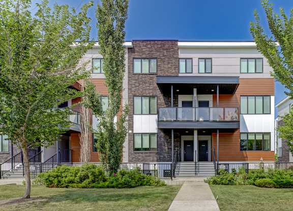 A modern multi-story apartment building with a balcony on the second floor.