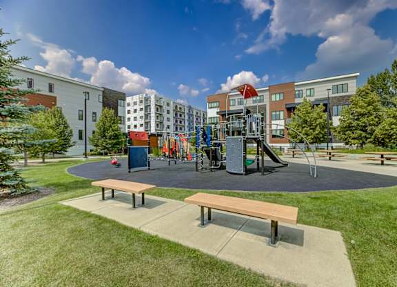 A playground with a slide and swings in front of a building.