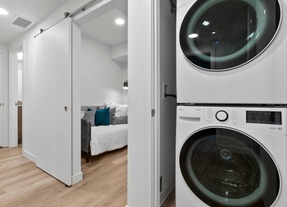 a washer and dryer in a laundry room with a bed in the background