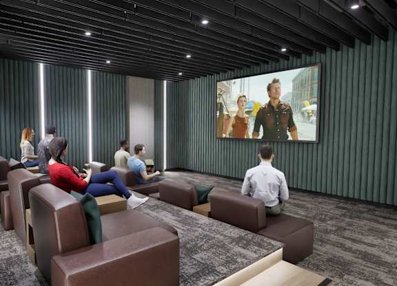 A group of people are sitting in a room with a large screen on the wall.