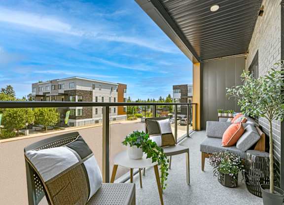 A balcony with a table, chairs, and potted plants overlooks a building.
